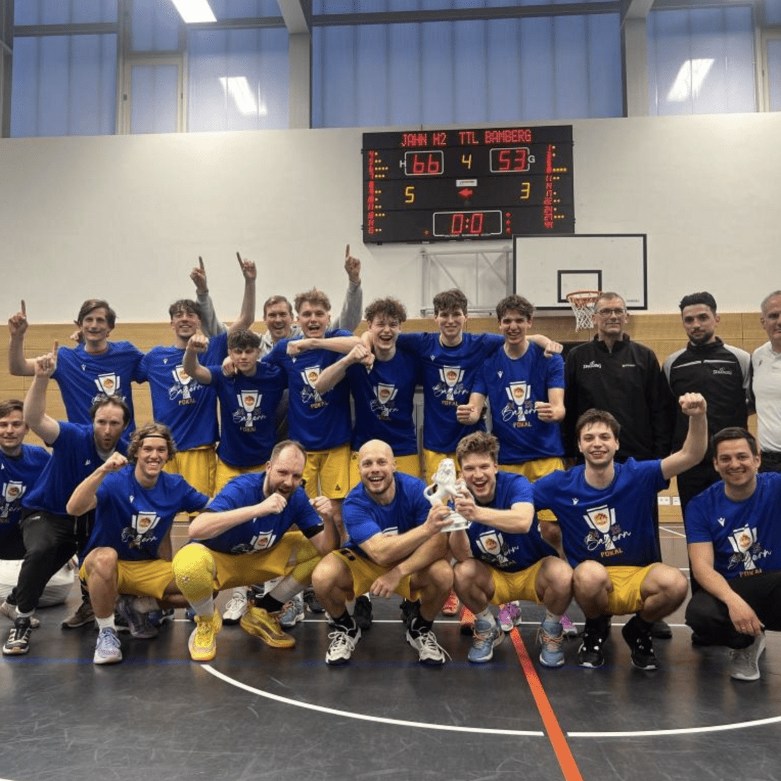 Mannschaft aus zw&ouml;lf Basketballspielern in blauen T-Shirts, jubelnd nach einem Sieg auf dem Spielfeld.
