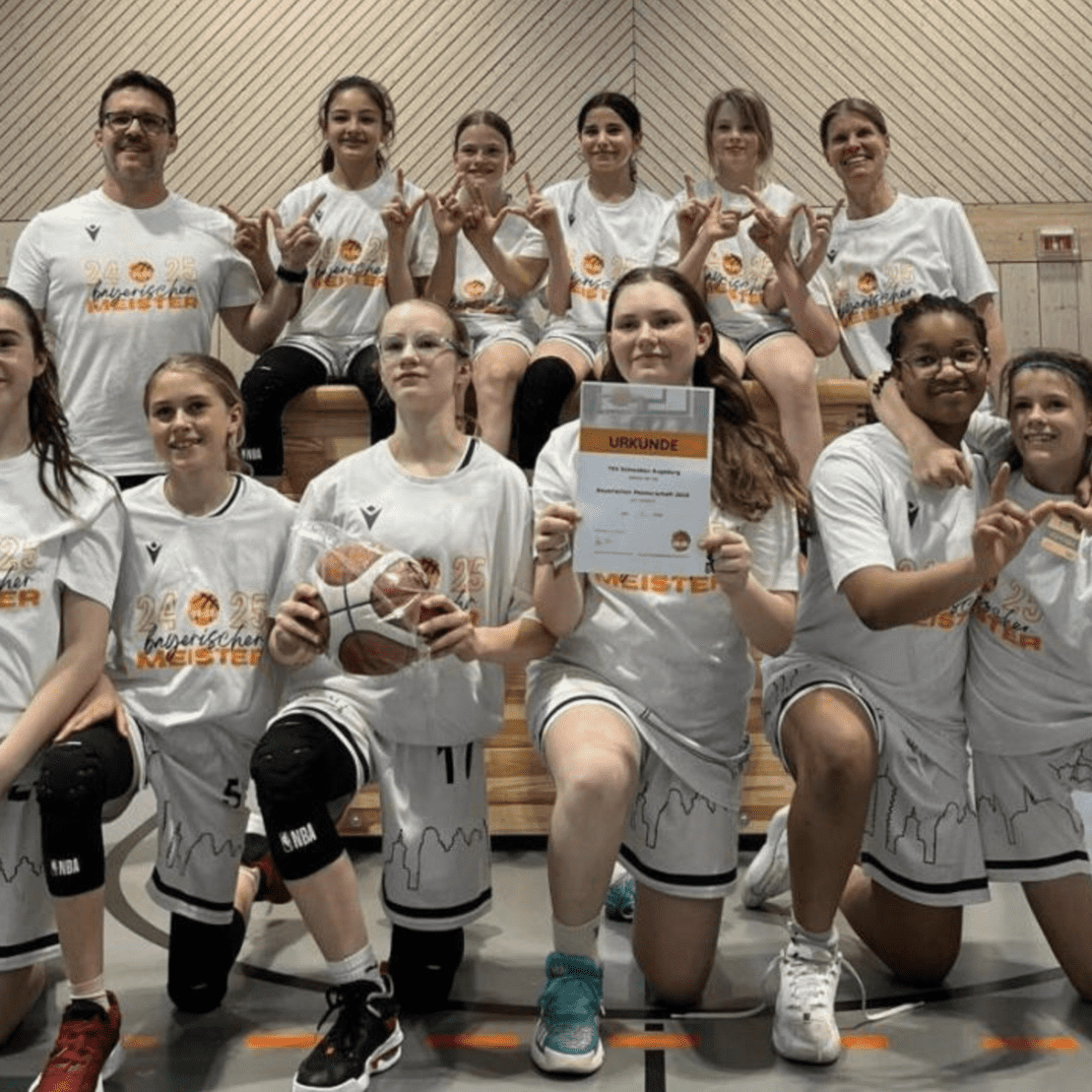 Gruppenshot eines Basketballteams in wei&szlig;en T-Shirts, stolz mit Urkunde und Basketball auf einem Holzblock.