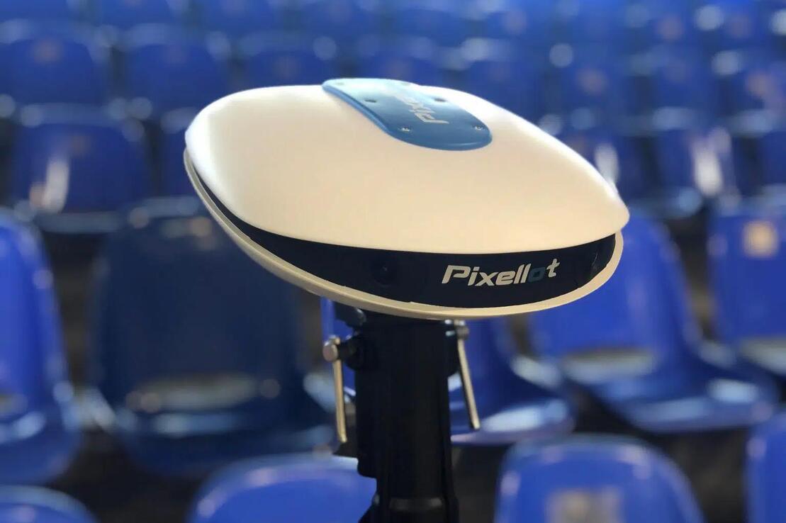 Kamera von Pixellot auf einem Stativ, vor einer Reihe blauer Zuschauerpl&auml;tze in einer Sportarena.