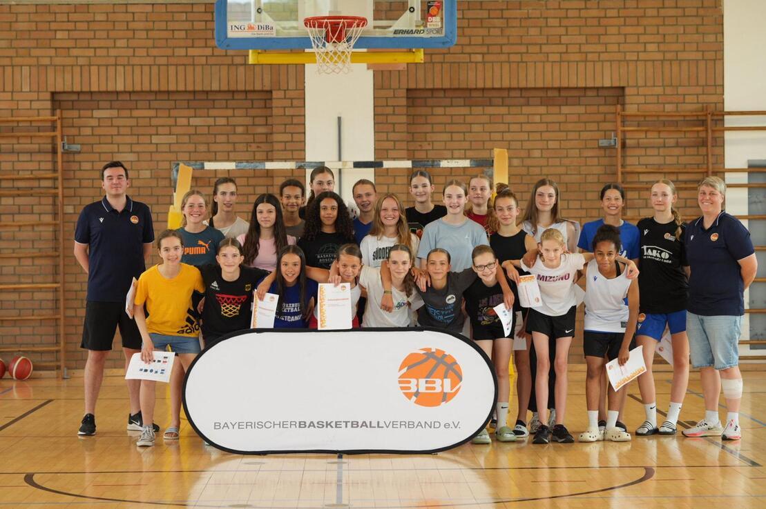 Gruppe von Jugendlichen und Trainern im Basketballsport, stehend vor einem Banner des Bayerischen Basketballverbands.