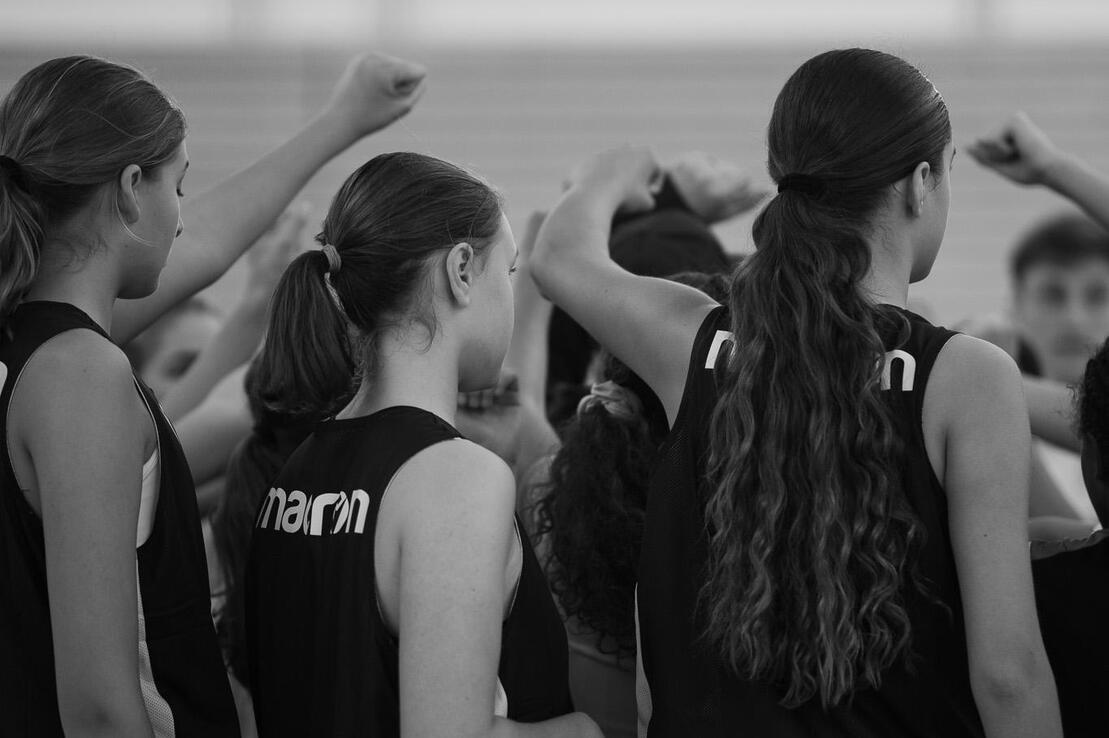 Gruppe junger Sportlerinnen in schwarzen Trikots versammelt sich, um einen motivierenden Moment gemeinsam zu erleben.