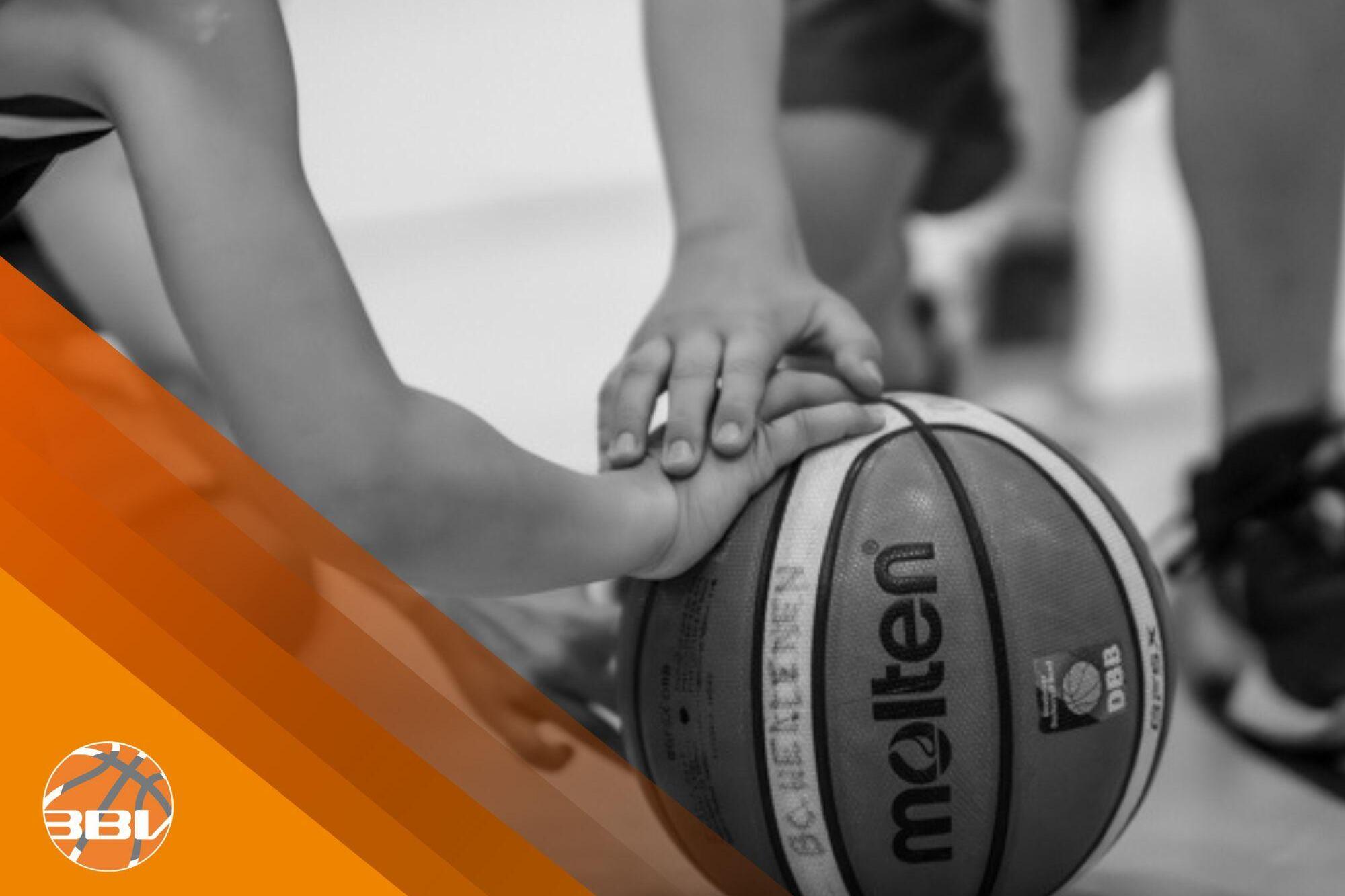 Nahaufnahme von H&auml;nden, die einen Basketball auf dem Boden halten, mit orangefarbenem Design im Bildhintergrund.