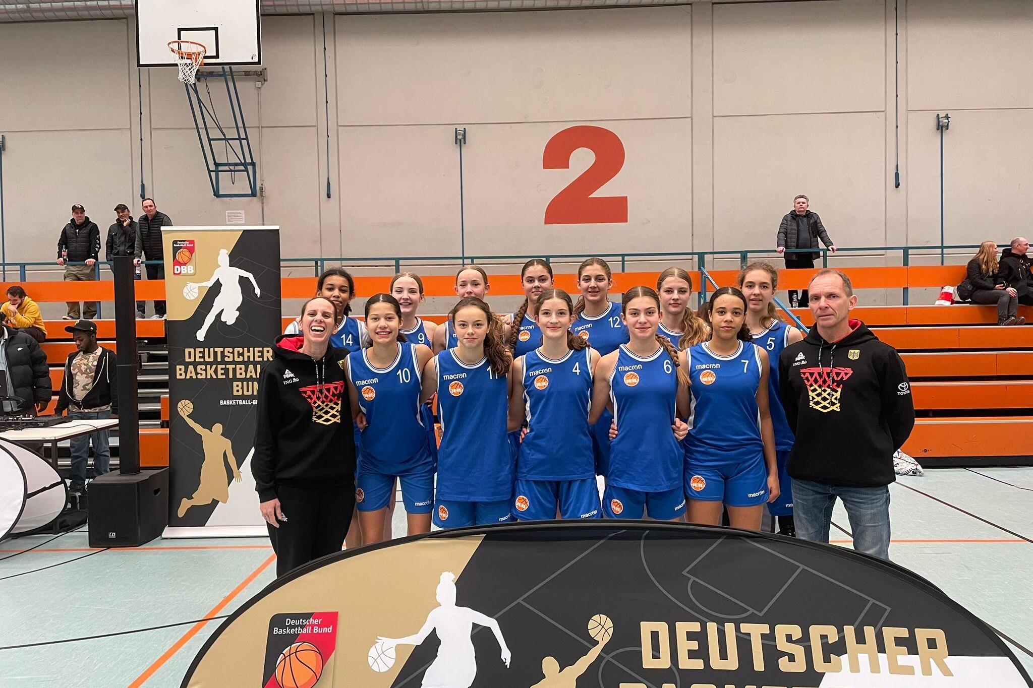 Mannschaftsbild einer Basketballjugend mit Trainer, vor einem Banner des Deutschen Basketball Bundes in einer Halle.