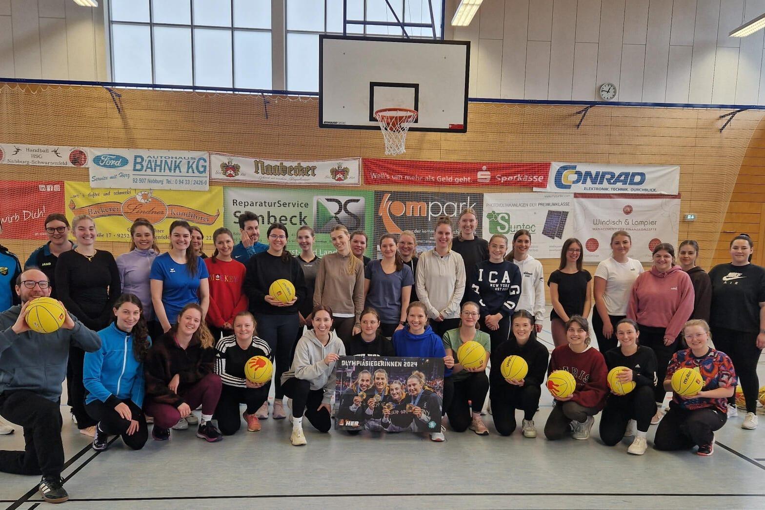 Gruppenbild von Frauen und einem Mann in Sportbekleidung, die mit gelben Bällen in einer Sporthalle posieren.
