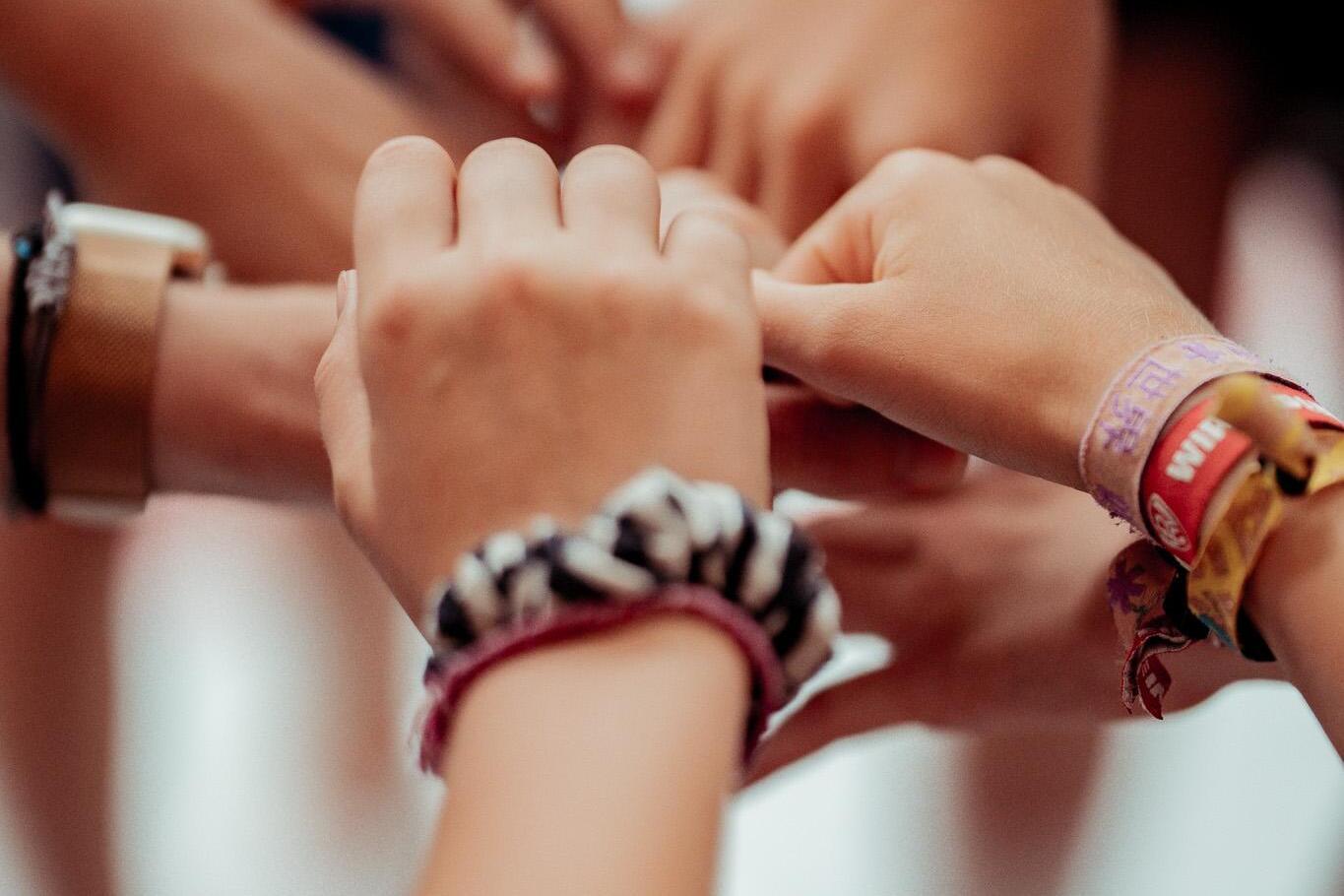 H&auml;nde verschiedener Personen legen sich &uuml;bereinander, viele Armb&auml;nder sind sichtbar. Hintergrund unscharf.