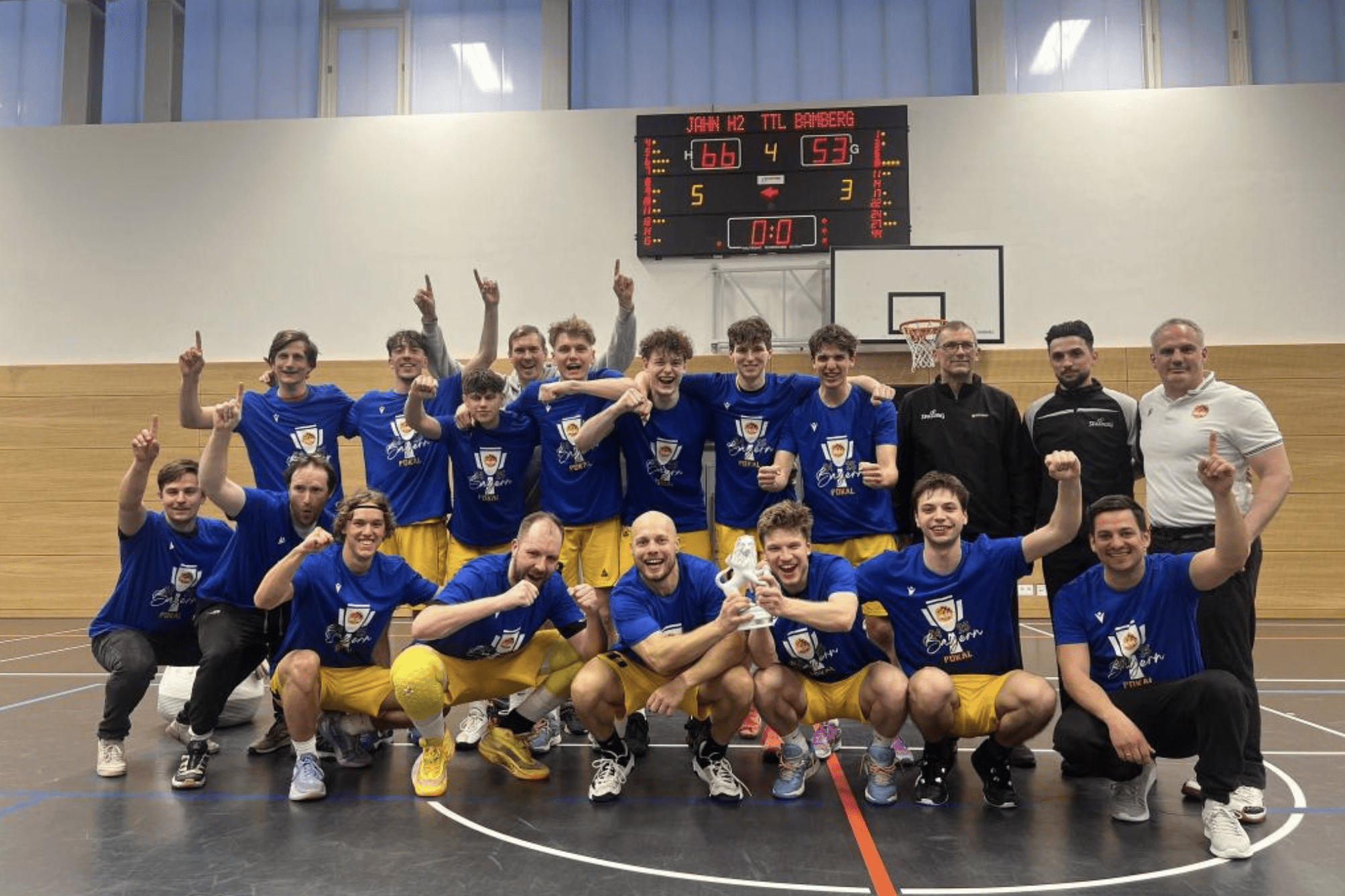 Mannschaft aus zw&ouml;lf Basketballspielern in blauen T-Shirts, jubelnd nach einem Sieg auf dem Spielfeld.