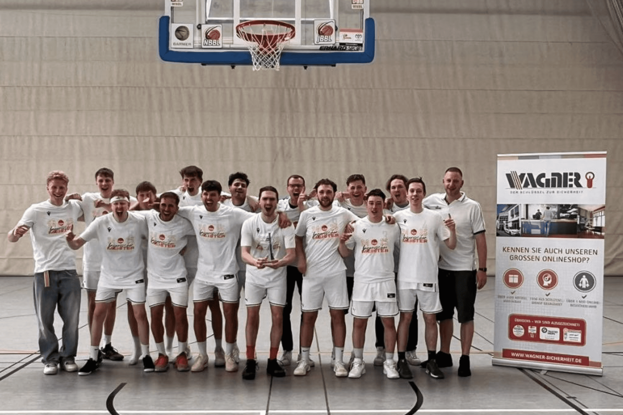 Gruppe von Basketballspielern in wei&szlig;en Trikots posiert vor einem Werbebanner in einer Sporthalle.