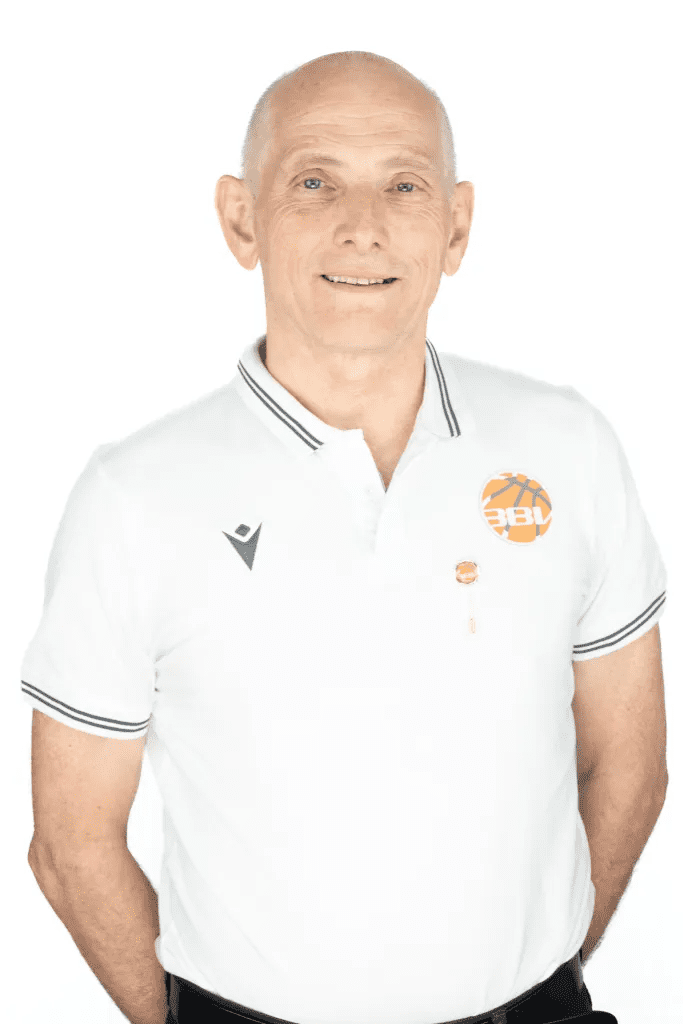 Portr&auml;t eines l&auml;chelnden Mannes mit kurzen, grauen Haaren, in einem wei&szlig;en Poloshirt mit Basketball-Logo.