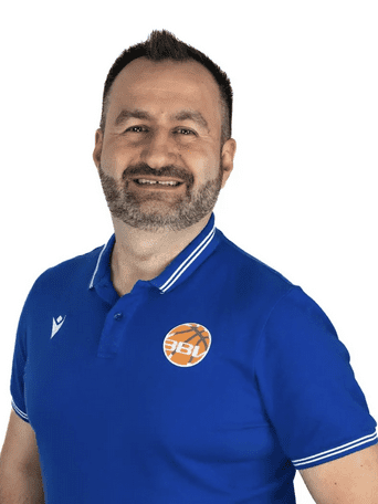 Mann mit Bart in blauer Sportpoloshirt l&auml;chelt vor wei&szlig;em Hintergrund.