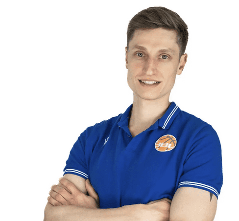 L&auml;chelnder Mann mit kurzen Haaren, tr&auml;gt ein blaues Shirt mit Logo und hat die Arme vor der Brust verschr&auml;nkt.