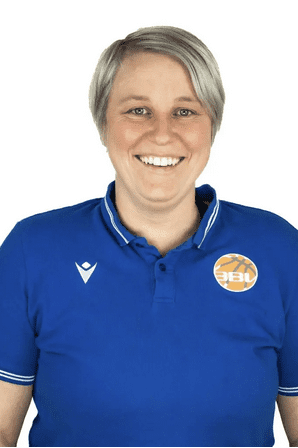 L&auml;chelnde Frau mit kurzer blonder Frisur tr&auml;gt ein blaues Polohemd mit einem Vereinslogo auf der Brust.