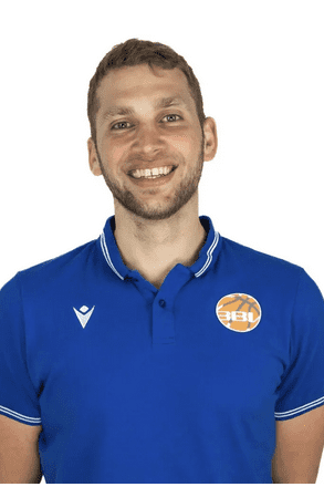 L&auml;chelnder Mann mit kurzem, lockigem Haar tr&auml;gt ein blaues Poloshirt mit Logo. Hintergrund ist einfarbig wei&szlig;.