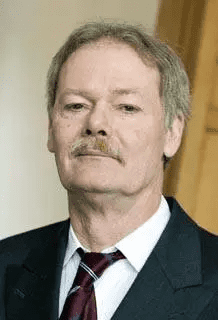 Portr&auml;t eines Mannes mit grauen Haaren und Schnurrbart, gekleidet in Anzug mit Krawatte, ernsthaft und nachdenklich schauend.