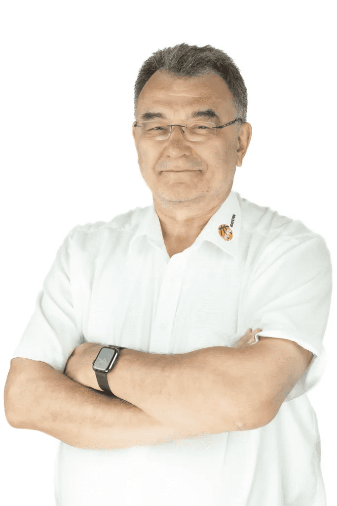 Portrait eines l&auml;chelnden Mannes mit Brille, in wei&szlig;em Hemd, die Arme vor der Brust verschr&auml;nkt, auf hellem Hintergrund.