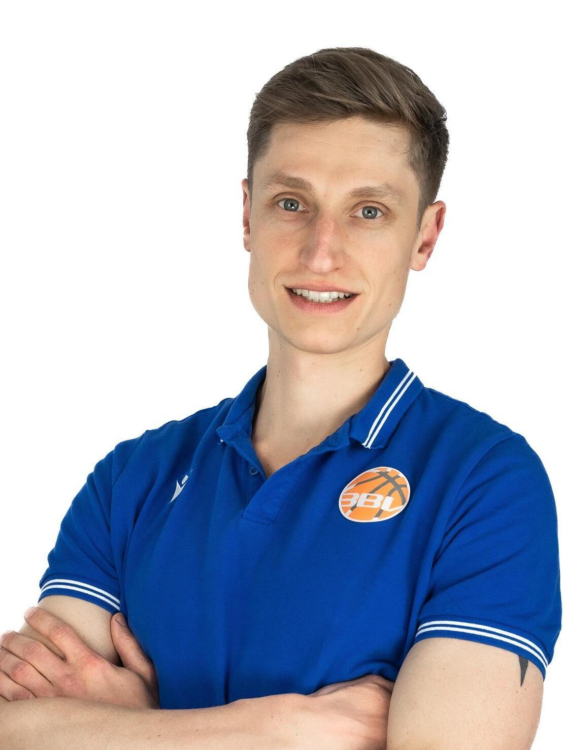 Mann mit kurzem Haar in blauem Poloshirt steht mit verschr&auml;nkten Armen vor wei&szlig;em Hintergrund.